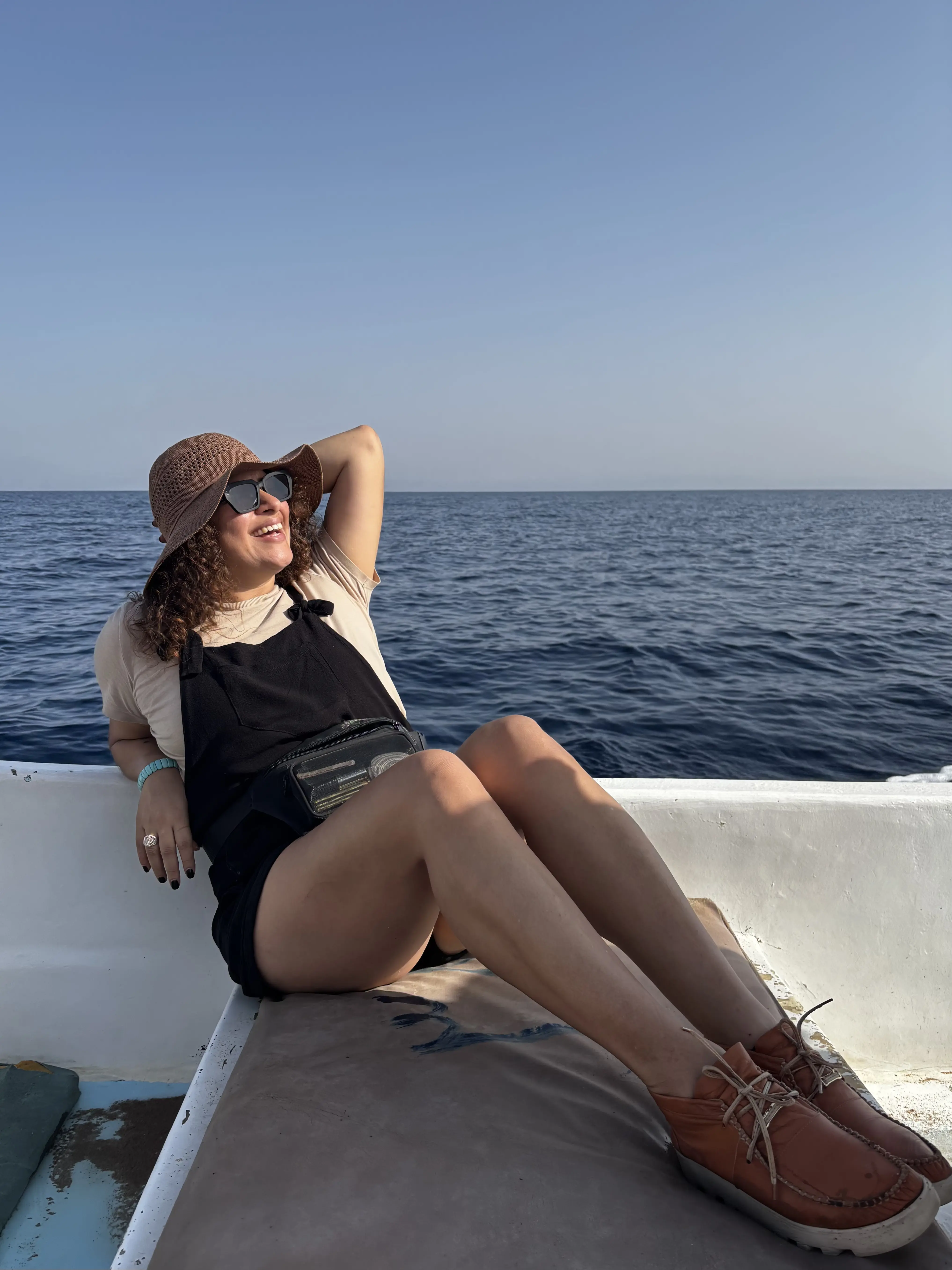 Rosi sitting on a boat in a sun hat, with open blue sea behind her