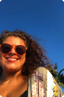 Rosi smiling in sunlight, wearing sunglasses beneath a blue sky